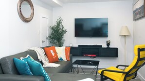 Una sala moderna con un sofá gris, un sillón amarillo, un televisor de pantalla plana, un mueble de entretenimiento negro y una lámpara de pie.