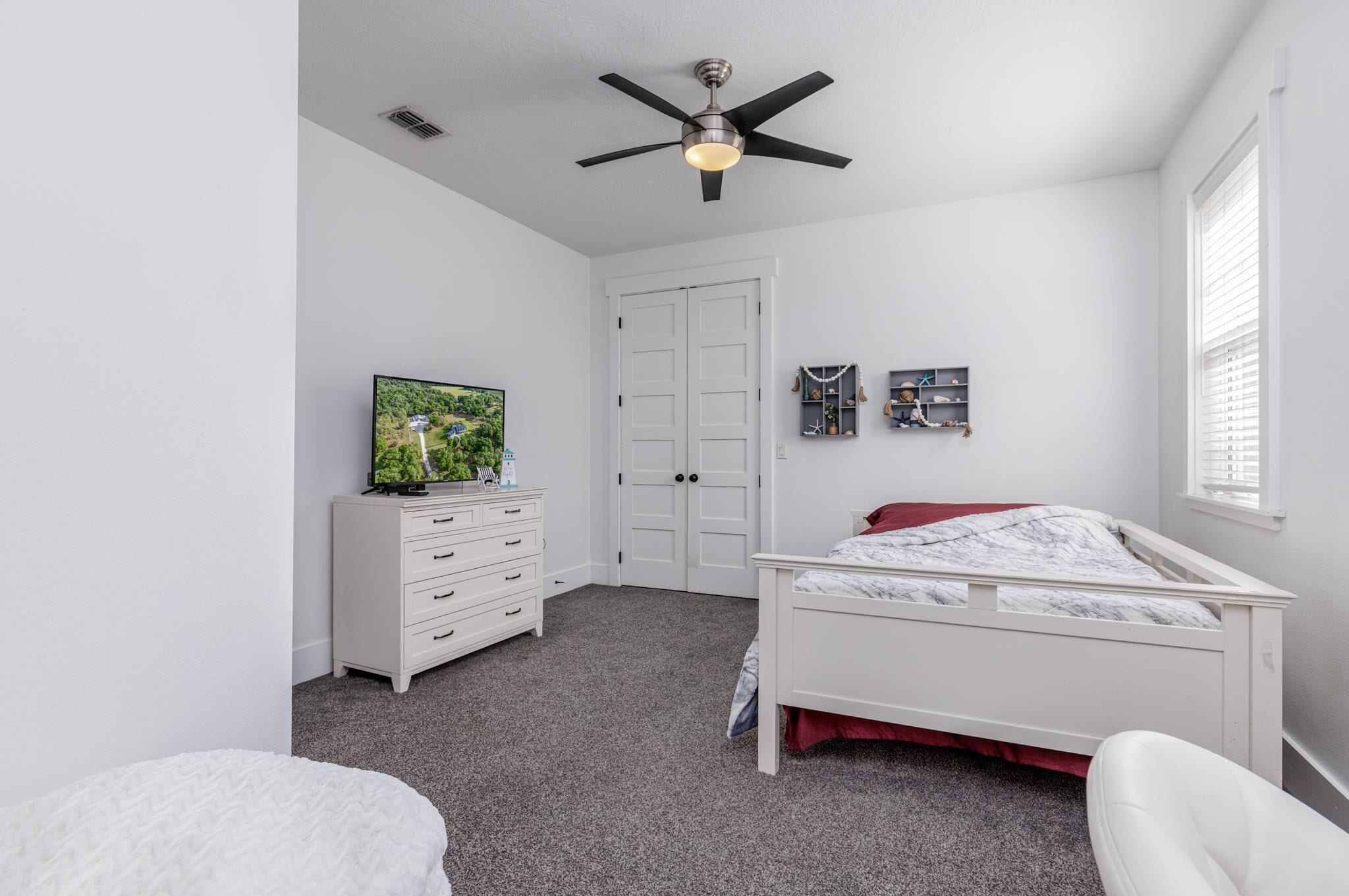 Un dormitorio con cama, cómoda, ventilador de techo y televisor.