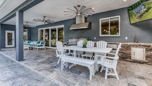 Eine Außenpatio mit Grill, Sitzgelegenheiten und Deckenventilatoren.