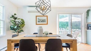 Un coin repas avec une table en bois, des chaises noires, un luminaire suspendu aux motifs géométriques, une plante en pot et un tableau encadré au mur.