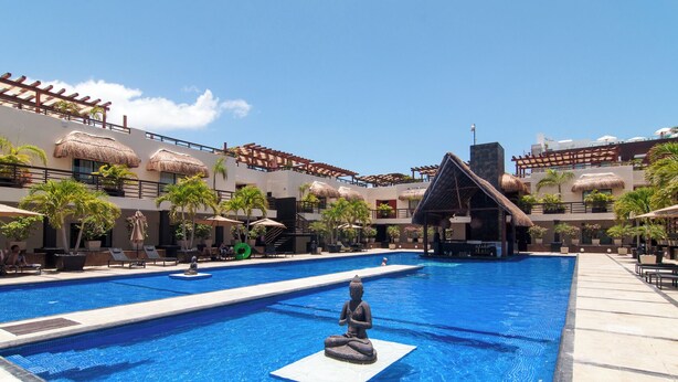 A large outdoor swimming pool with a statue in the center, surrounded by lounge chairs and umbrellas.