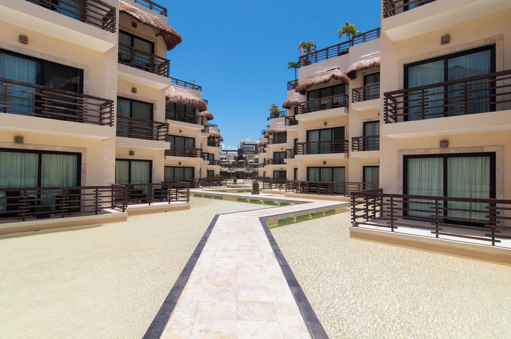 A resort with multiple-story buildings, balconies with thatched roofs, and a central courtyard.