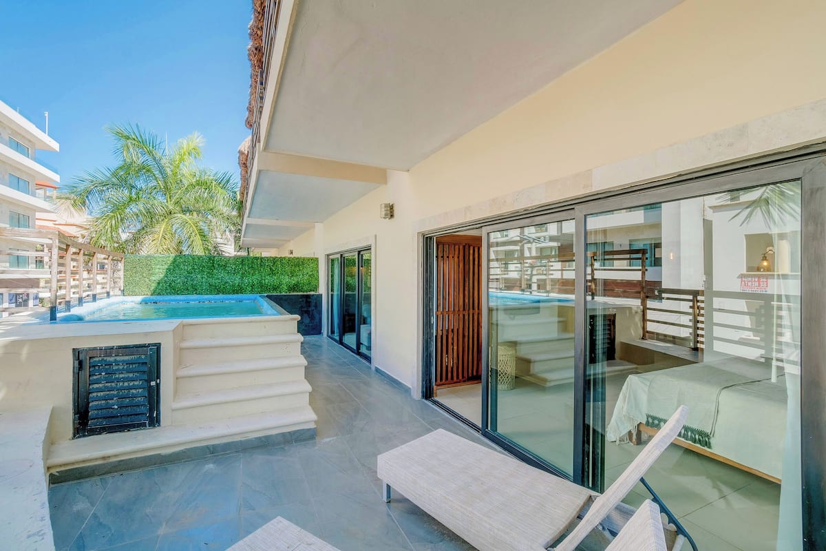 A modern hotel suite with a glass door leading to a balcony, a small pool, and a bed with a view.