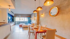 A modern dining area with a wooden table set for four, surrounded by chairs. There are pendant lights above the table, and a round mirror on the wall.