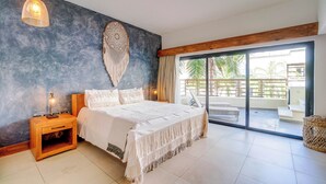 A bedroom with a large bed, a nightstand, a wall hanging, and a view of the outside balcony.