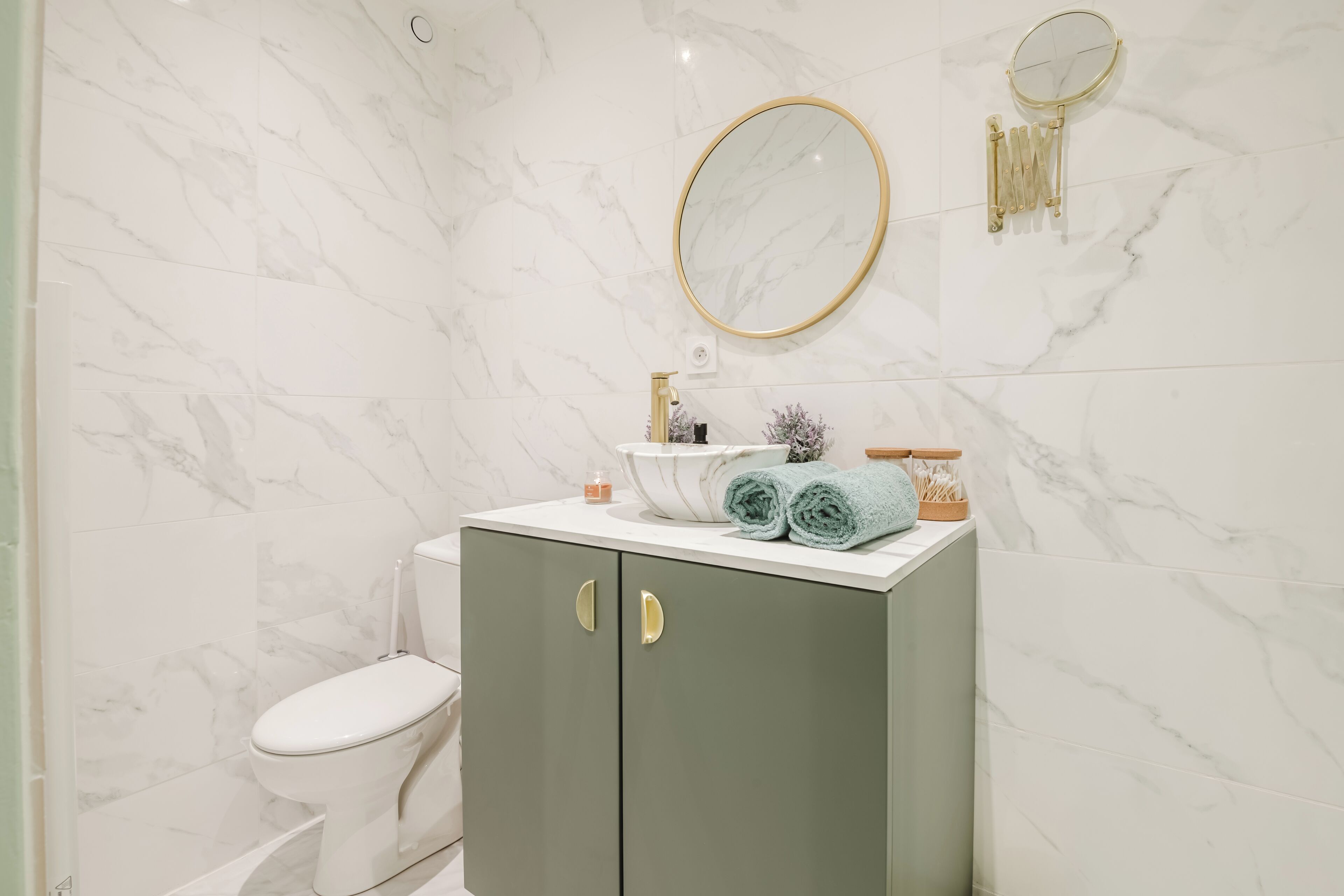 A bathroom with a toilet, a vanity with a mirror, and marble walls.
