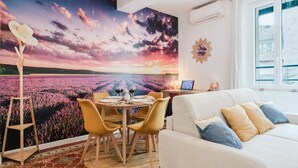 Een eetgedeelte met een tafel voor twee personen, een witte bank en een groot raam met uitzicht op een veld.