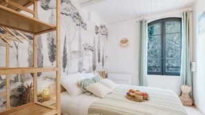 Een slaapkamer met een bed, een houten plank, een raam met gordijnen en een muur met een mural over de natuur.