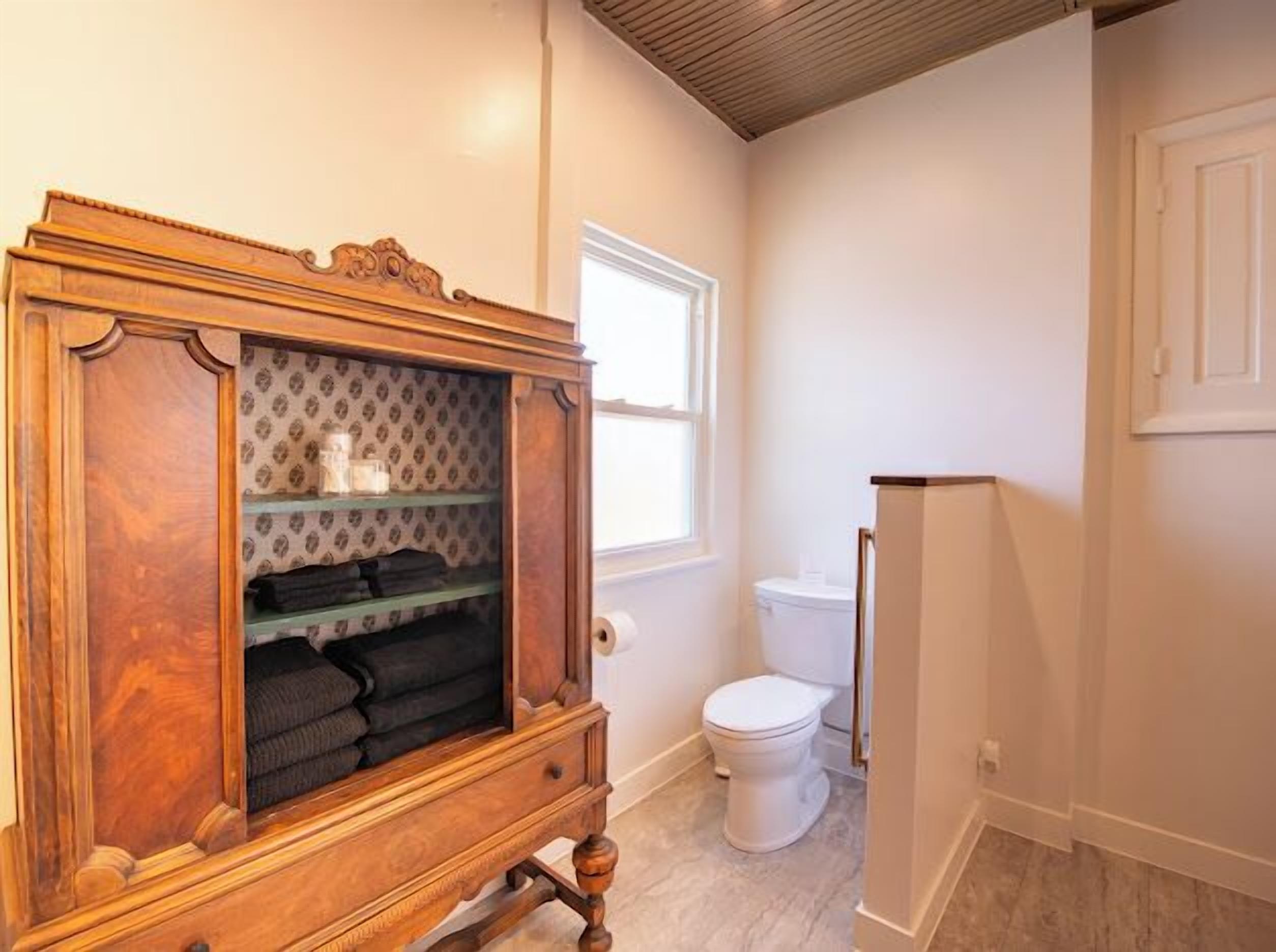 Ein Badezimmer mit einem Holzkosmetikschrank, einer Toilette und einem Fenster.