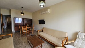 A living room with a sofa, wooden chairs, a coffee table, a TV, and a fireplace. - 74 LCA - Stay Sea Gate Apartment (Larnaca)