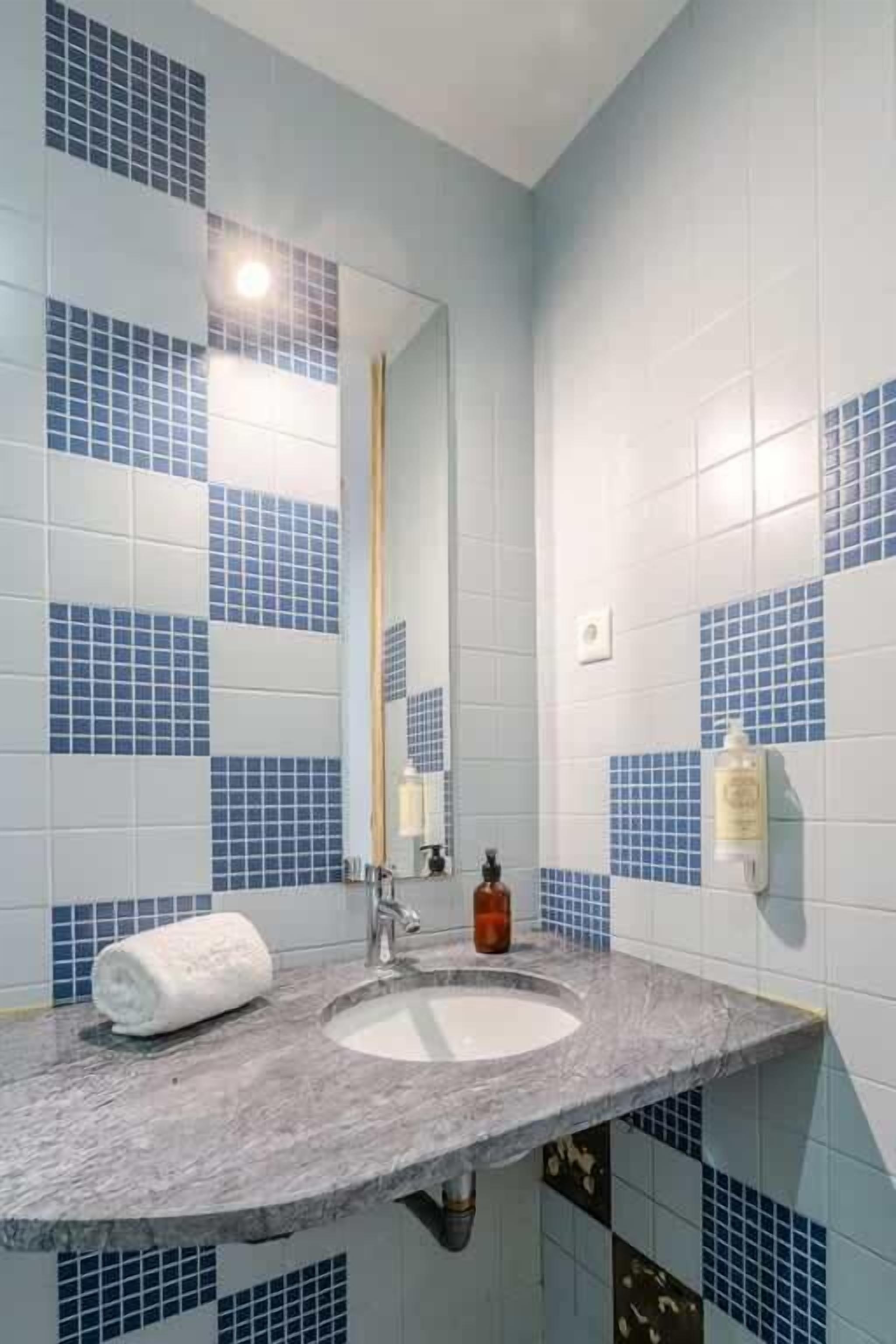 A bathroom with a sink, mirror, and blue-tiled walls.