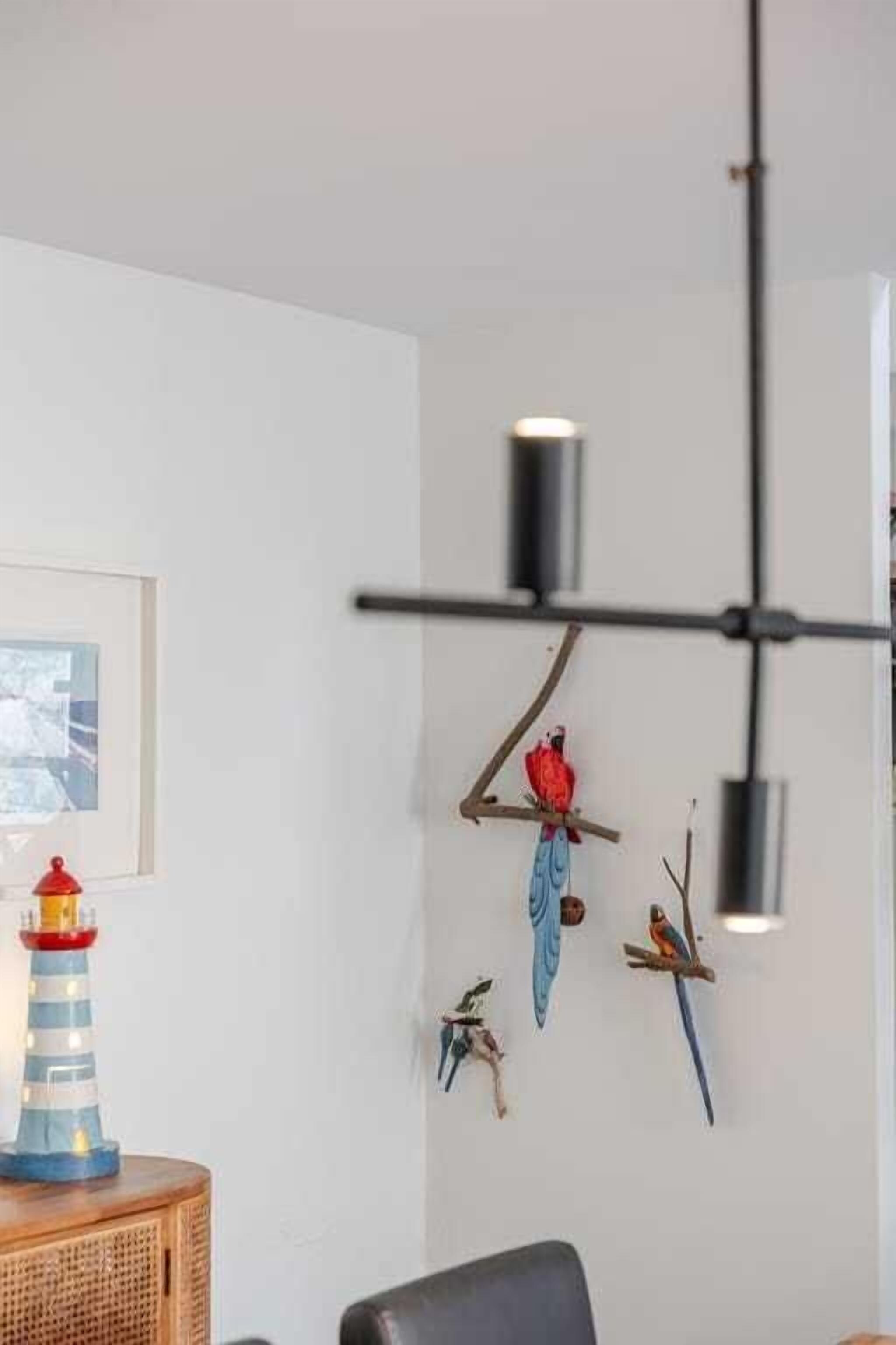 A room with a framed picture, a small table with a lighthouse model, a black chair, and wall-mounted bird decorations.
