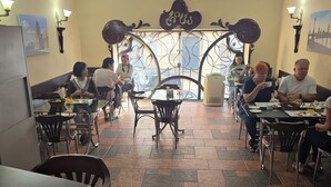 A restaurant with multiple tables and chairs, a tiled floor, and a decorative archway. - RITSA HOTEL (Batumi)