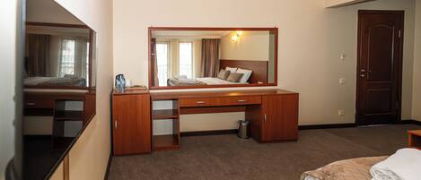 A hotel room with a bed, a desk, a mirror, a trash can, and a door.