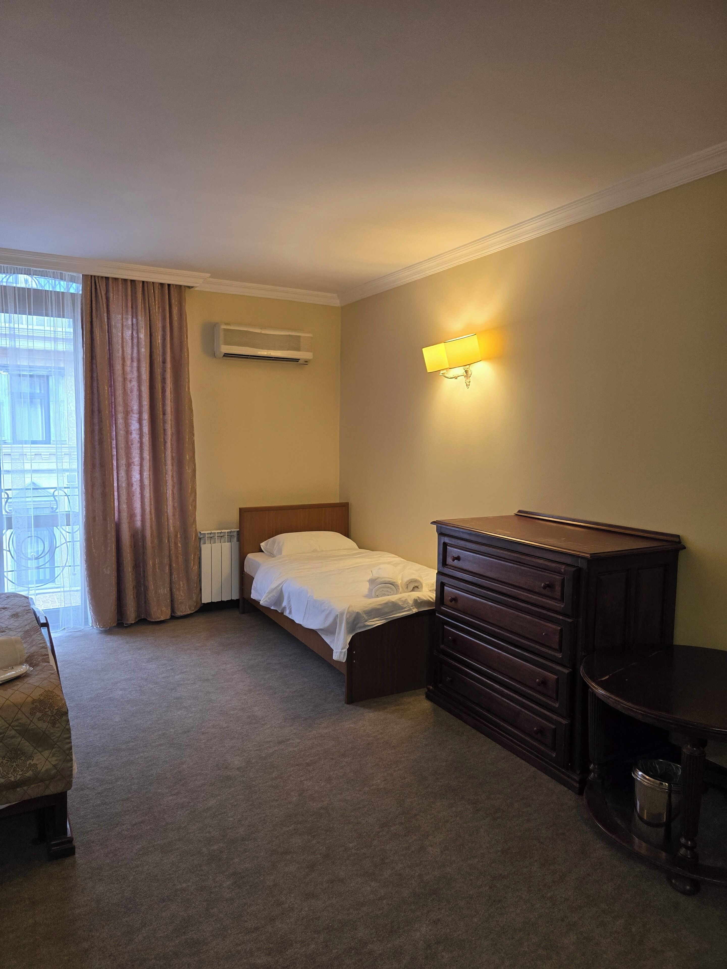 A hotel room with a bed, a dresser, a radiator, and a window with curtains.