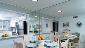 Une cuisine moderne dotée d’un grand îlot central, d’un coin repas avec une table ronde et des chaises, et d’un mur miroitant qui reflète la cuisine.