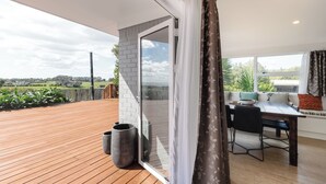 Un patio moderno con terraza de madera, una puerta corrediza de vidrio que da a un balcón y un área de comedor con mesa y sillas.