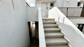 A narrow stairway leading to a white door, flanked by white walls and a metal railing.