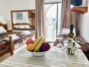 A hotel room with a bed, a dining table with a bowl of fruit, wine glasses, and a bottle of wine. - 79 AN - Stay Nissi Chrysland Studio 215 (Ayia Napa)