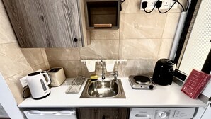 Eine kompakte Küchenzeile mit Spüle, Toaster, Wasserkocher, Kaffeemaschine und Waschmaschine.