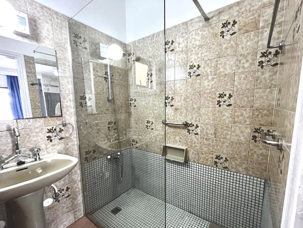 Une salle de bain avec un lavabo, un miroir, une douche et des murs carrelés ornés de motifs floraux.
