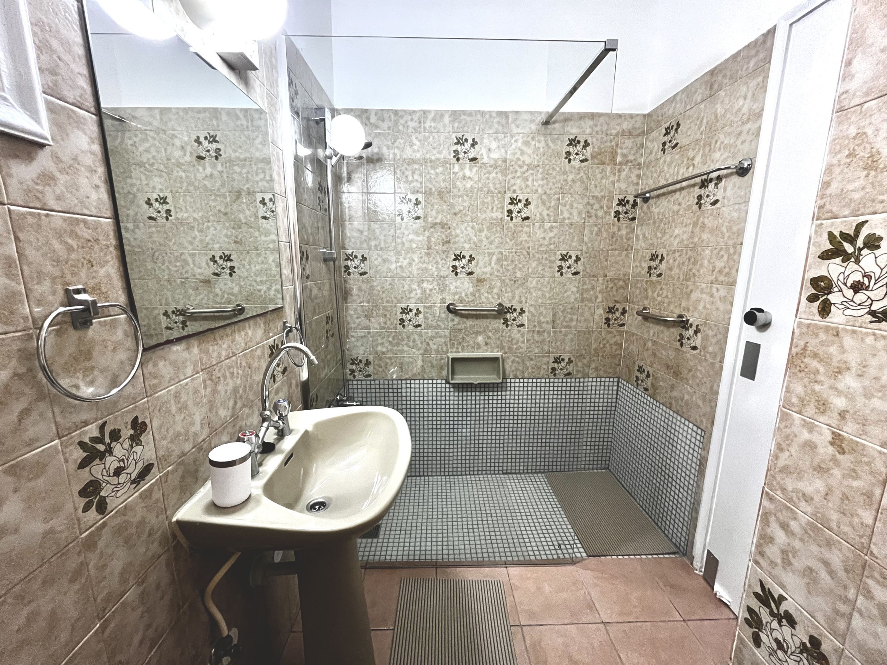 A bathroom with a sink, mirror, shower, and tiled walls.