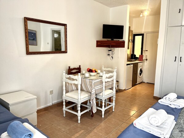 A small, clean room with a bed, a table with chairs, a mirror, a TV, and a washing machine.