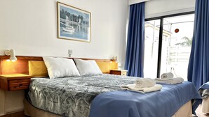 Ein ordentlich bezogenes Bett mit einem gemusterten Überwurf, zwei Nachttischlampen und einem gerahmten Bild an der Wand.