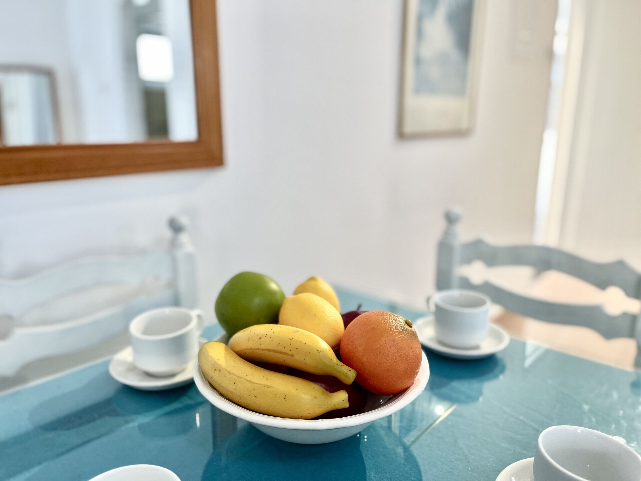 Una mesa con un bol de fruta y dos tazas blancas.
