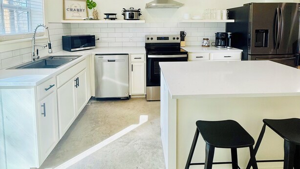 Una cocina moderna con armarios blancos, estufa de acero inoxidable, horno empotrado y una isla grande con taburetes de bar.