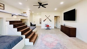 Una sala de estar moderna con una escalera, un televisor de pantalla plana y un ventilador de techo.