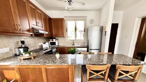 A kitchen with wooden cabinets, granite countertops, a stainless steel refrigerator, and a dining area with wooden chairs.