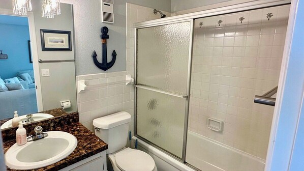 Een badkamer met een wit toilet, een wastafel met een marmeren aanrechtblad en een douche met glazen wanden.