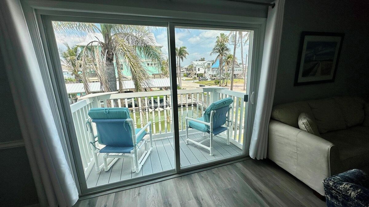 A room with a sliding glass door leading to a balcony with two chairs and a white couch.