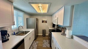A compact kitchen with white cabinets, a stainless steel refrigerator, a coffee maker, and a trash can.