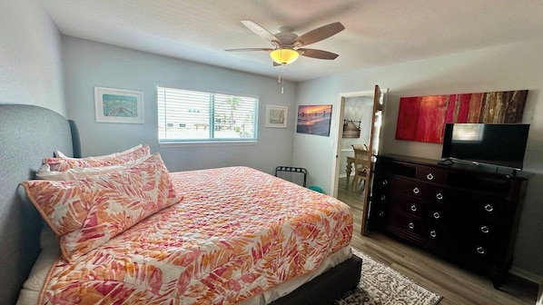 A bedroom with a bed, a dresser, a ceiling fan, and artwork on the walls.