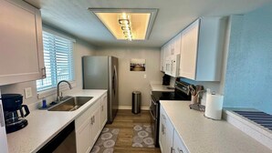 A compact kitchen with a stainless steel refrigerator, a coffee maker, and a trash can. - The Lighthouse - Steps from Beach (Fort Myers Beach)