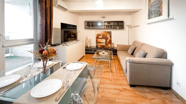 A modern living room with a glass dining table set for two, a sofa, and a TV. - Poznań Grunwald - 51m2, Balcony - by Rentujemy (Poznan)