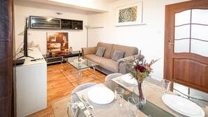 A modern living room with a sofa, a dining table set for two, and a kitchen area in the background. - Poznań Grunwald - 51m2, Balcony - by Rentujemy (Poznan)