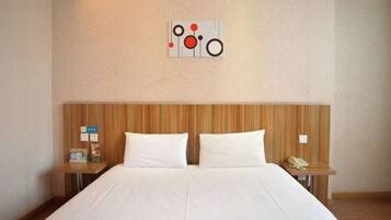Quarto de hotel com cabeceira de madeira, cama grande com roupa de cama branca, duas mesas de cabeceira e uma obra de arte pendurada na parede.