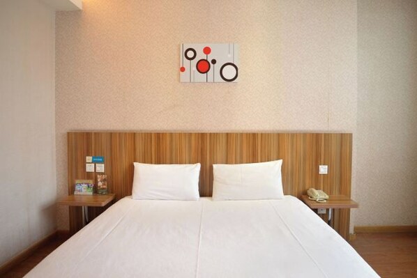 Una habitación de hotel con cabecera de madera, una cama grande con ropa de cama blanca, dos mesitas de noche y una obra de arte colgada en la pared.