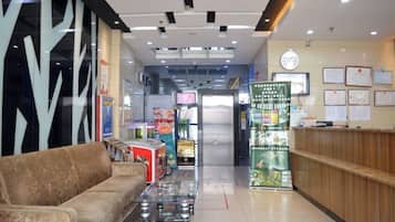 A hotel lobby with a reception desk, a sofa, vending machines, and a glass coffee table.