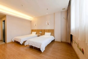 Habitación de hotel con dos camas individuales, piso de madera, una mesita de noche y televisor instalado en la pared.