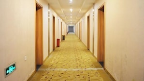 A long, narrow hotel corridor with wooden doors on both sides, a patterned carpet, and a green exit sign on the left wall. - Lin Luo Hotel (Shijiazhuang Time Street) (Shijiazhuang)