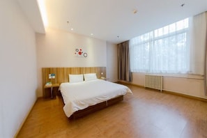 Habitación de hotel con una cama grande, cabecera de madera, mesita de noche, una obra de arte en la pared y un amplio ventanal con cortinas.