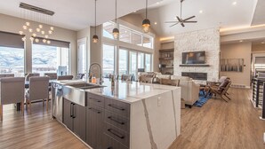 A spacious kitchen with a large island, modern pendant lighting, and a stone fireplace. - Mountains and Horses and Deer, Oh My! (Heber City)