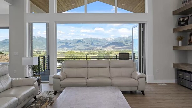 A spacious living room with a large window offering a mountain view, a beige sofa, and a coffee table. - Mountains and Horses and Deer, Oh My! (Heber City)