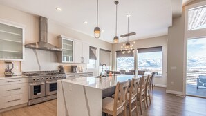 A modern kitchen with a large island, stainless steel appliances, and a view of mountains through large windows. - Mountains and Horses and Deer, Oh My! (Heber City)