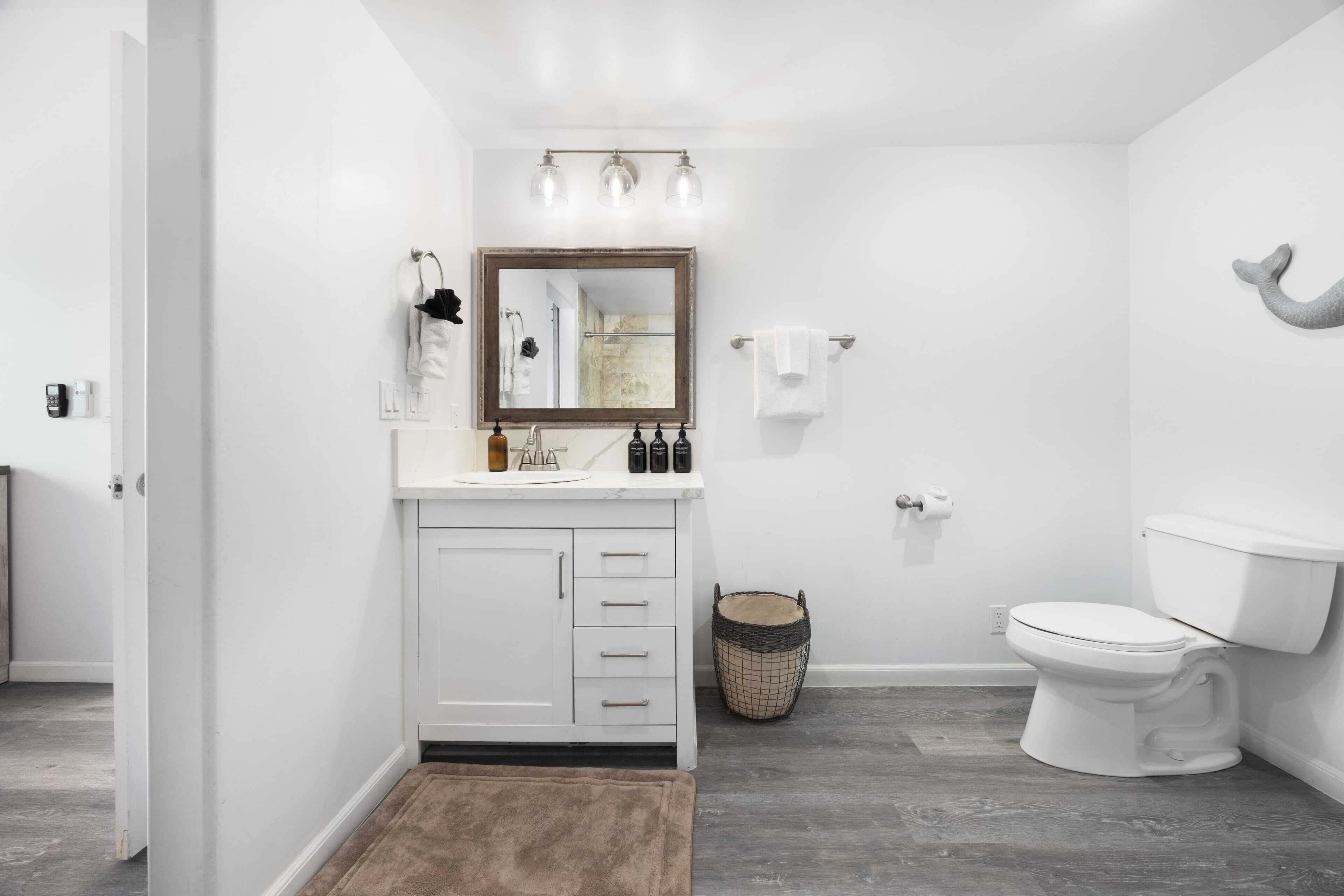 A bathroom with a white vanity, a mirror, a toilet, and a shower area.