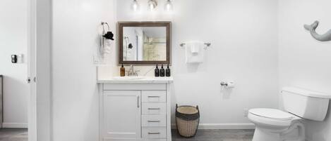 A bathroom with a white vanity, a mirror, a toilet, and a shower area.